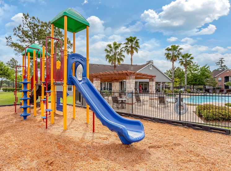 Colorful Playground  on Mulch with Building Exterior and Fenced in Pool in the Background